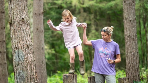 A mother holds her daughter's hand as she balances on logs at the natural play area at Calke Abbey, Derbyshire